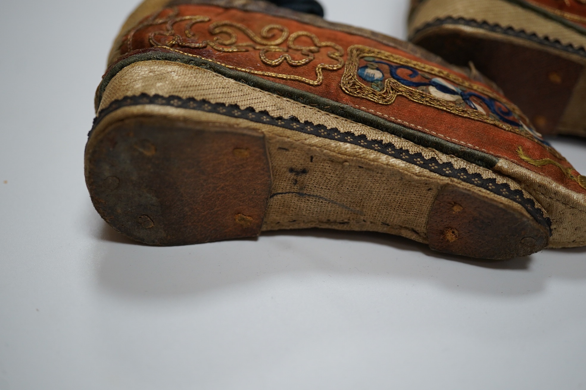 A pair of Chinese silk and gold thread embroidered ladies shoes, with leather binding around the top and gold brocade platform heels with fine blue braiding, 12cm long. Condition - good for age and use